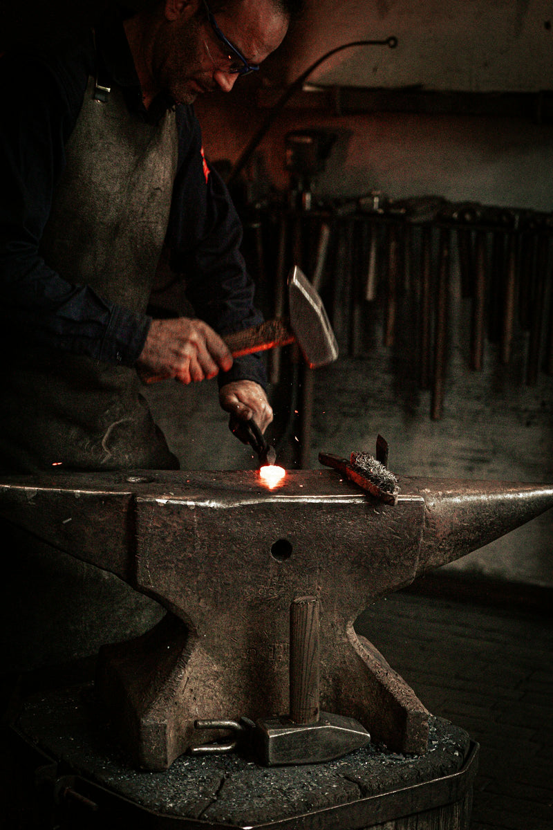 Blacksmith working on a piece of metal with a hammer at the anvil